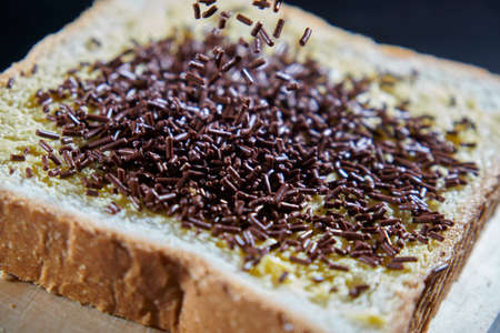 Chocolate sprinkles on a slice of plain bread spread with butter.の写真素材