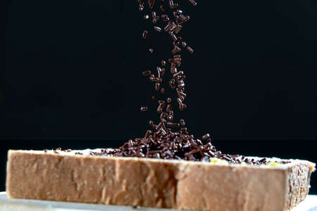 Chocolate sprinkles poured onto the bread, isolated on black background.の写真素材