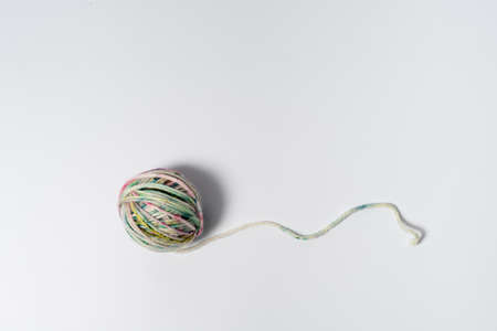 Small ball of light multicolored yarn with a loose string on white background