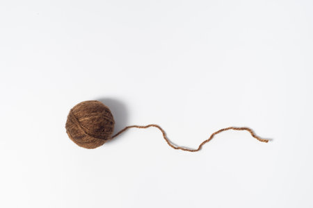 Dark brownish ball of yarn with loose thread on white backgroundの写真素材