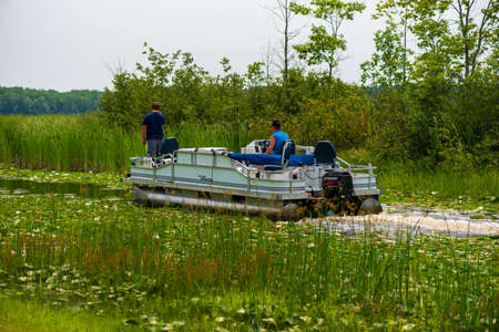 Alpena Michigan, USA - July 18, 2021: Pontoon boat navigating a narrow canalのeditorial素材