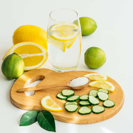 sliced cucumber and orange on a wooden board, a spoon with salt and a glass with water and lemonの写真素材