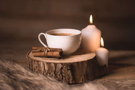 white cup of coffee, candles,cinnamon and fur on a wooden backgroundの写真素材