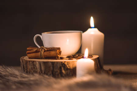 white cup of coffee, candles,cinnamon, fur and coffee beans on a wooden backgroundの写真素材