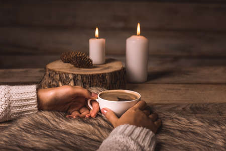 white cup with coffee in the hands of a girl,  fur, cones and candles on a wooden backgroundの写真素材