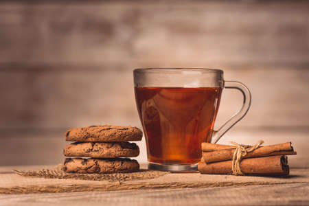 a cup with tea, cookies and cinnamon  on a wooden background