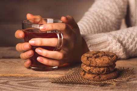 cup of black tea in the hands of a girl and cookies on the table on a wooden backgroundの写真素材