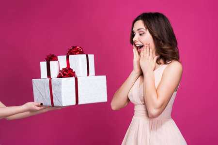 surprised brunette in a pink dress takes a lot of gifts, on a pink backgroundの写真素材