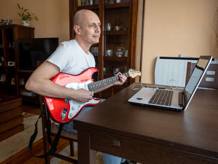 Young man at home taking online electric guitar classes