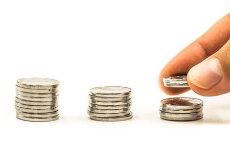 piles of coins on white background with a hand putting extra coinsの写真素材