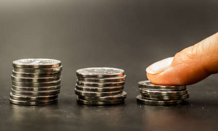 piles of coins on black background with a hand putting extra coinsの写真素材