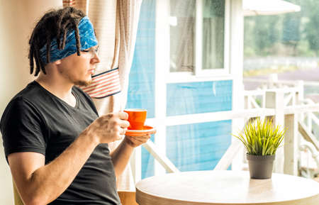 a man with dreadlocks is drinking tea looking to the windowの写真素材
