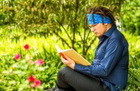 young man with dreadlocks reads a book in a parkの写真素材