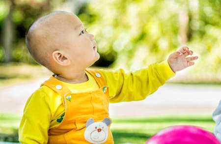 a baby sits on the mat in the park stretching a handの写真素材