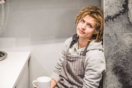 Young hipster woman sitting with a white cup in the kitchenの写真素材