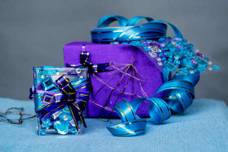 Christmas craft composition on the blue tablecloth. candle with gems and blue ribbon, a gift and Xmas tree decorationsの写真素材