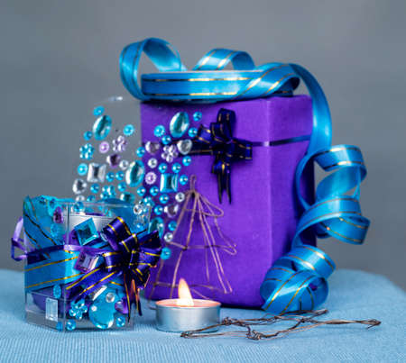 christmas craft composition on the blue tablecloth. candle with gems and blue ribbon, a gift and xmas tree decorationsの写真素材