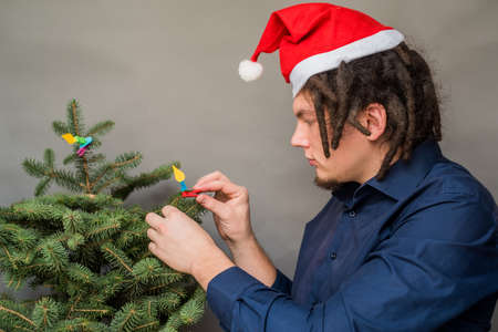 young european man with afro hairstyle and santa hat haning decorations on charistmas treeの写真素材