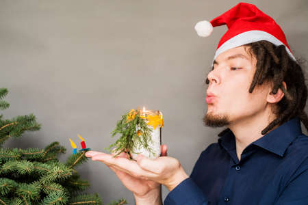 young european man in christmas hat blowing at a candle and christmas tree on the backgroundの写真素材