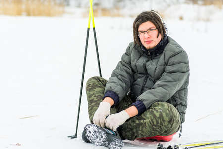 skier with ski equipment sitting on the snow in winter with snow fallingの写真素材