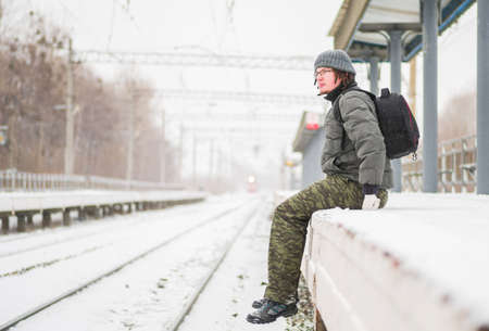 railway station outdoors in snow in winter. man waiting for a train with snow fallingの写真素材