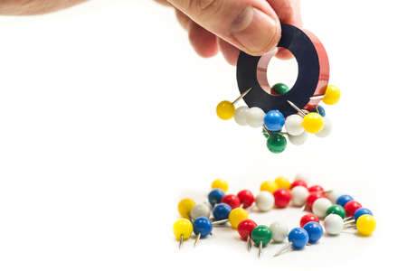 round red and blue magnet attracting metal paper pins in a hand isolated on whiteの写真素材
