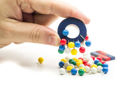 round red and blue magnet attracting metal paper pins in a hand isolated on whiteの写真素材