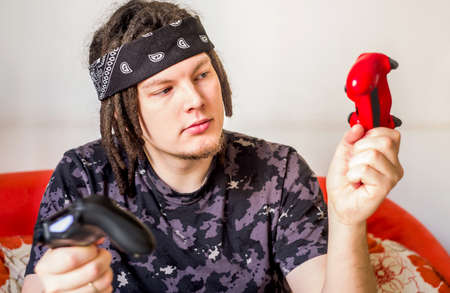 young caucasian man with dreadlocks sitting on the couch playing video gamesの写真素材