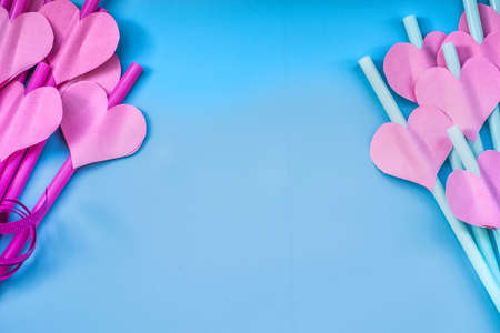 valentines day holiday. bright pink and blue drinking straws with hearts and a pink ribbon on blue.bright sipping straws for party or birthdayの写真素材
