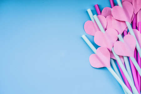 valentines day holiday. bright pink and blue drinking straws with hearts and a pink ribbon on blue.bright sipping straws for party or birthdayの写真素材