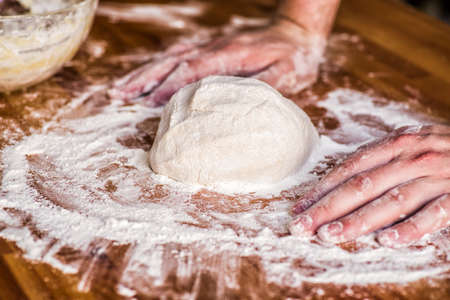 male hands kneading dough on wooden table. mass of dough on a tableの写真素材