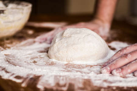 male baker hands kneading dough with flour on wooden tableの写真素材