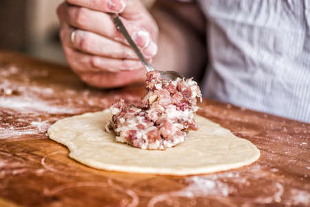 homemade raw meat pie on a wooden table. male hand filling a dumpling on a wooden surfaceの写真素材
