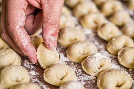 male hand putting a homemade dumpling on a wooden table covered with raws of dumplingsの写真素材