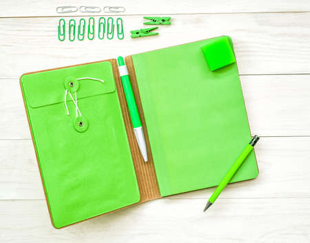 green notebook with eraser, pen,pencil and paper clips on white wooden backgroundの写真素材