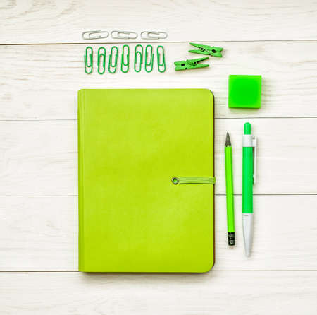 green notebook with eraser, pen,pencil and paper clips on white wooden background. creative set for dreawing,writing or making notesの写真素材
