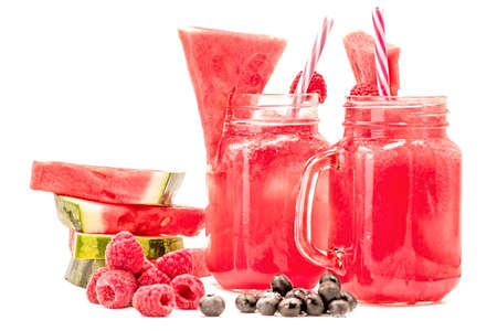 watermelon smoothie in a mason jar decorated with a slice of watermelon, raspberries ans ice cubes isolated on white background. fruit smoothie with a drinking straw isolatedの写真素材