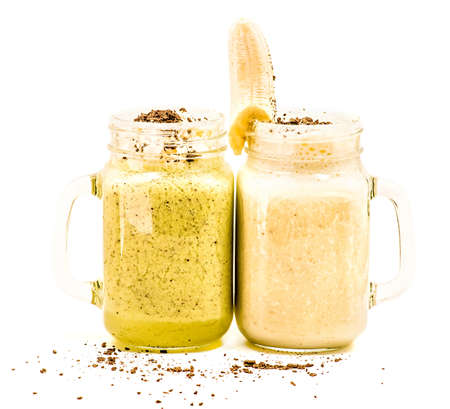 banana and kiwi milkshakes in mason jars with creme and chocolate on top decorated with banana isolated on whiteの写真素材