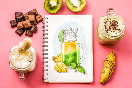two banana and kiwi milkshakes in mason jars with creme and chocolate chips on top decorated with kiwis and chocolate scatter. flat lay top view smoothies on pinkの写真素材