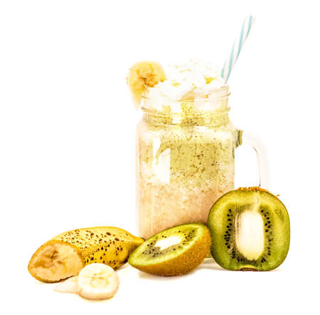 banana and kiwi milkshake in mason jar with creme on top and drinking straw decorated with slices of fruit isolated on whiteの写真素材
