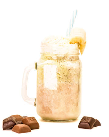 banana and kiwi milkshake in mason jar with creme on top and drinking straw decorated with chocolate isolated on whiteの写真素材
