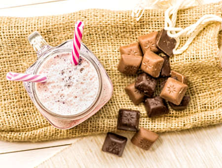 berry and fruit milkshake top view on white wooden background decorated with pieces of chocolate and coffee bag. summer drinks and desserts. fresh natural organic milkshake with two drinking straws flat layの写真素材