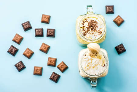 two banana and kiwi milkshakes in mason jars with creme on top decorated with chocolate pieces. flat lay top view smoothie on blue fashion background. creative layout with chocolate and milkshakesの写真素材
