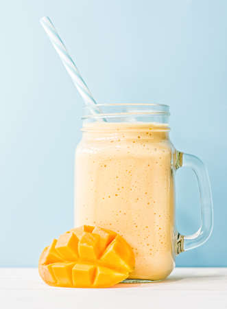 summer drink mango milkshake in mason jar with drinking straw decorated with a half of mango on blue backgroundの写真素材