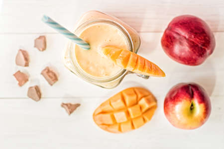 summer drink mango milkshake in mason jar with drinking straw decorated with a half of mango, chocolate pieces flat lay top view on white wooden backgroundの写真素材