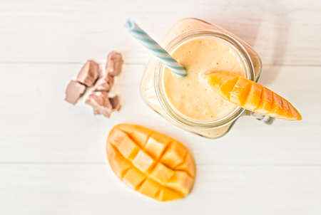 summer drink mango milkshake in mason jar with drinking straw decorated with a half of mango, chocolate pieces flat lay top view on white wooden backgroundの写真素材