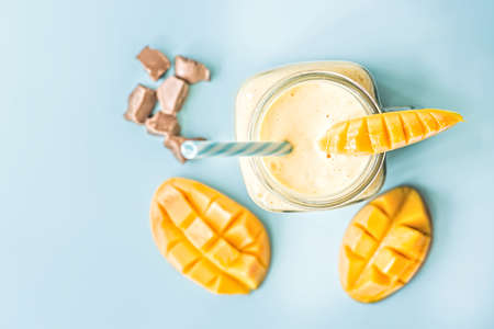 summer drink mango milkshake in mason jar with drinking straw decorated with a half of mango, chocolate pieces flat lay top view on white wooden backgroundの写真素材