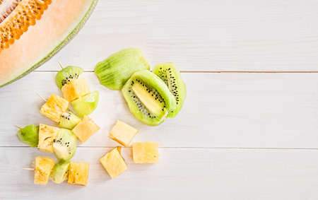 melon half with fruit canapes and kiwi slices on white wooden background flat top viewの写真素材
