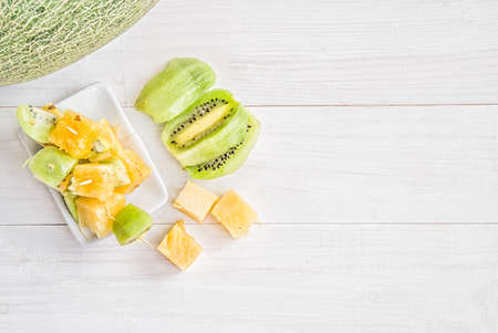 melon half with fruit canapes and kiwi slices on white wooden background flat top viewの写真素材