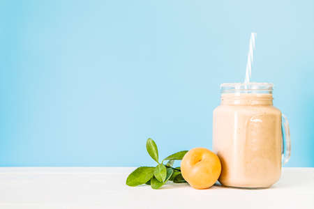 apricot milkshake decorated with fresh apricot and green leaves on white and blue backgroundの写真素材